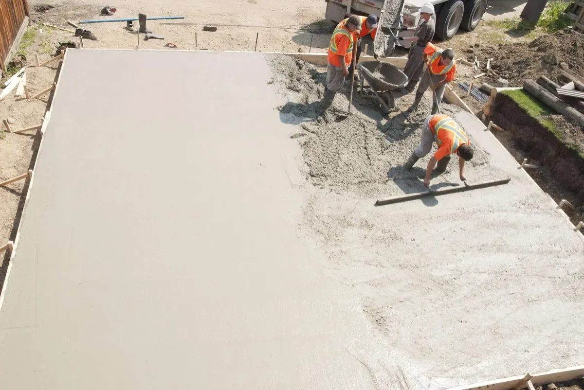 Crew placing and screeding a concrete slab inside wood forms