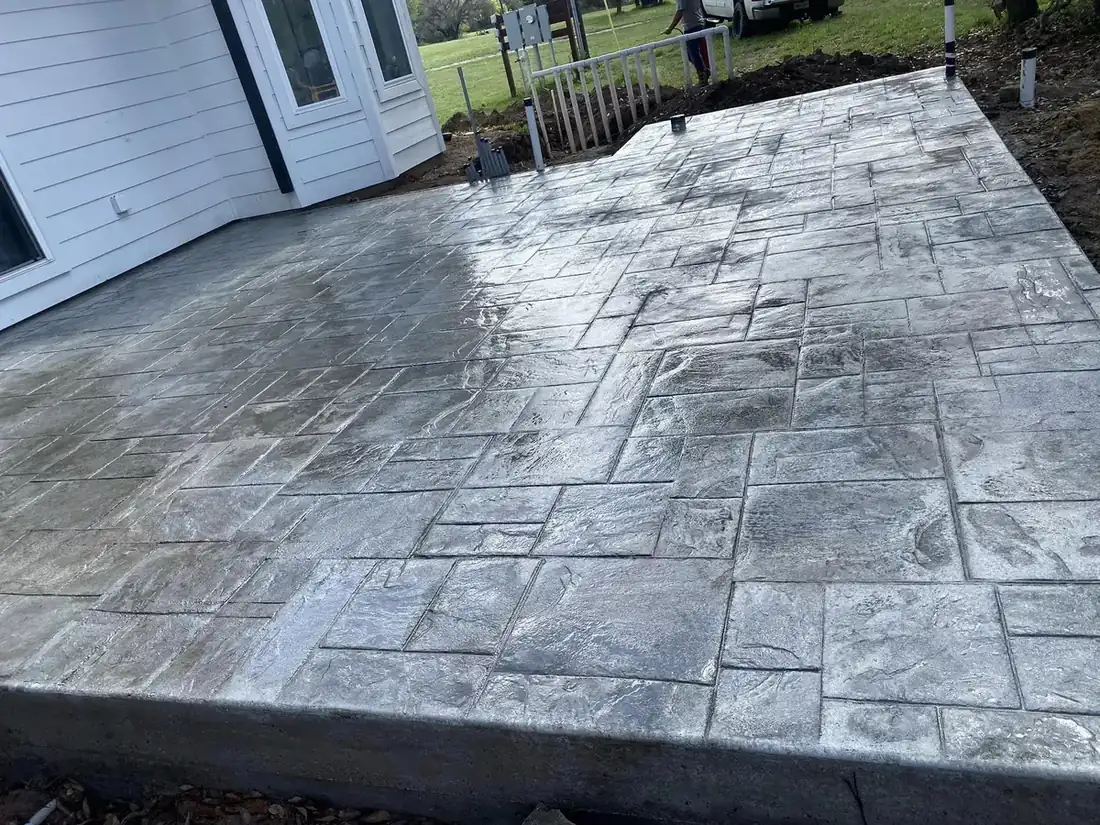 Gray stamped slate-pattern concrete patio beside a white house
