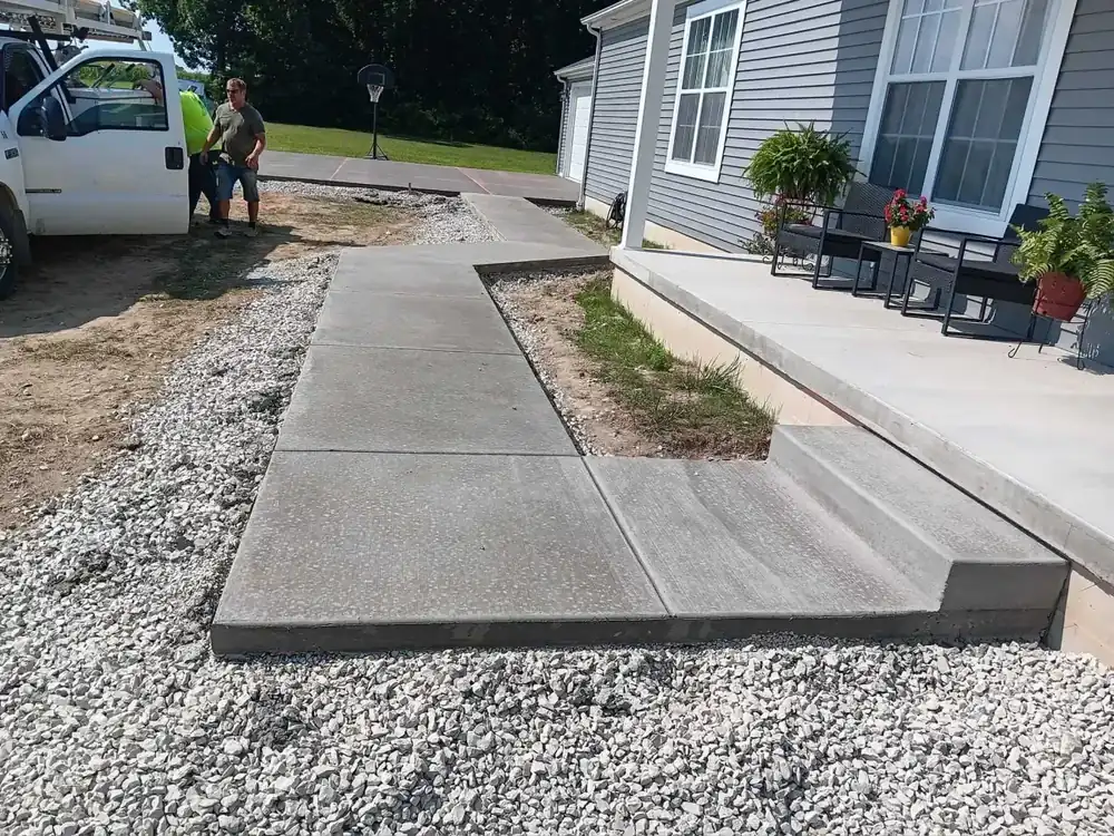 New broom-finish concrete walkway and step beside a house, set on a gravel base