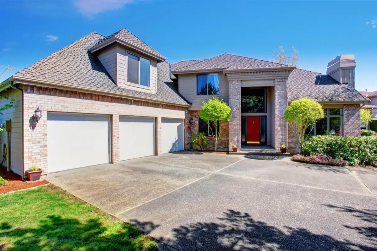 Wide concrete driveway in front of a brick home with a three-car garage